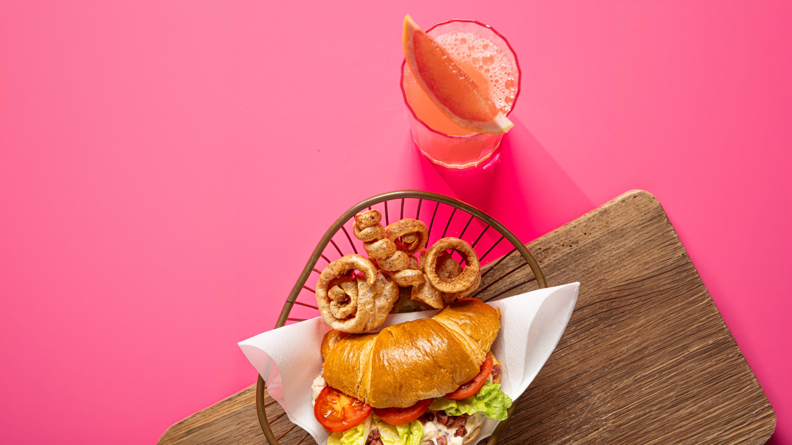Foodfotografie: Croissant-Sandwich mit Grapefruit-Drink auf pinkem Hintergrund